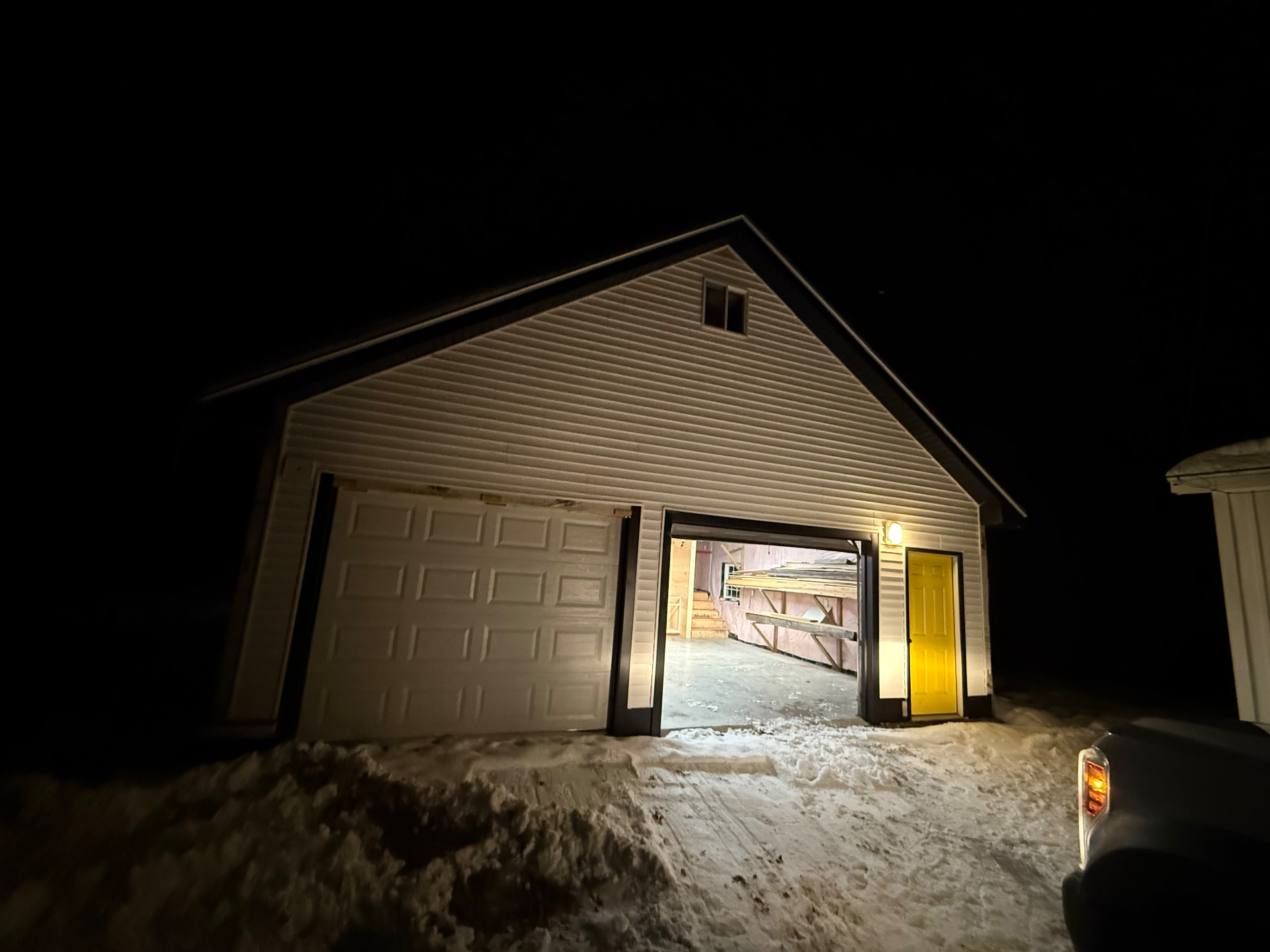 Finished garage exterior lit at night with new overhead door and entry door in the snow