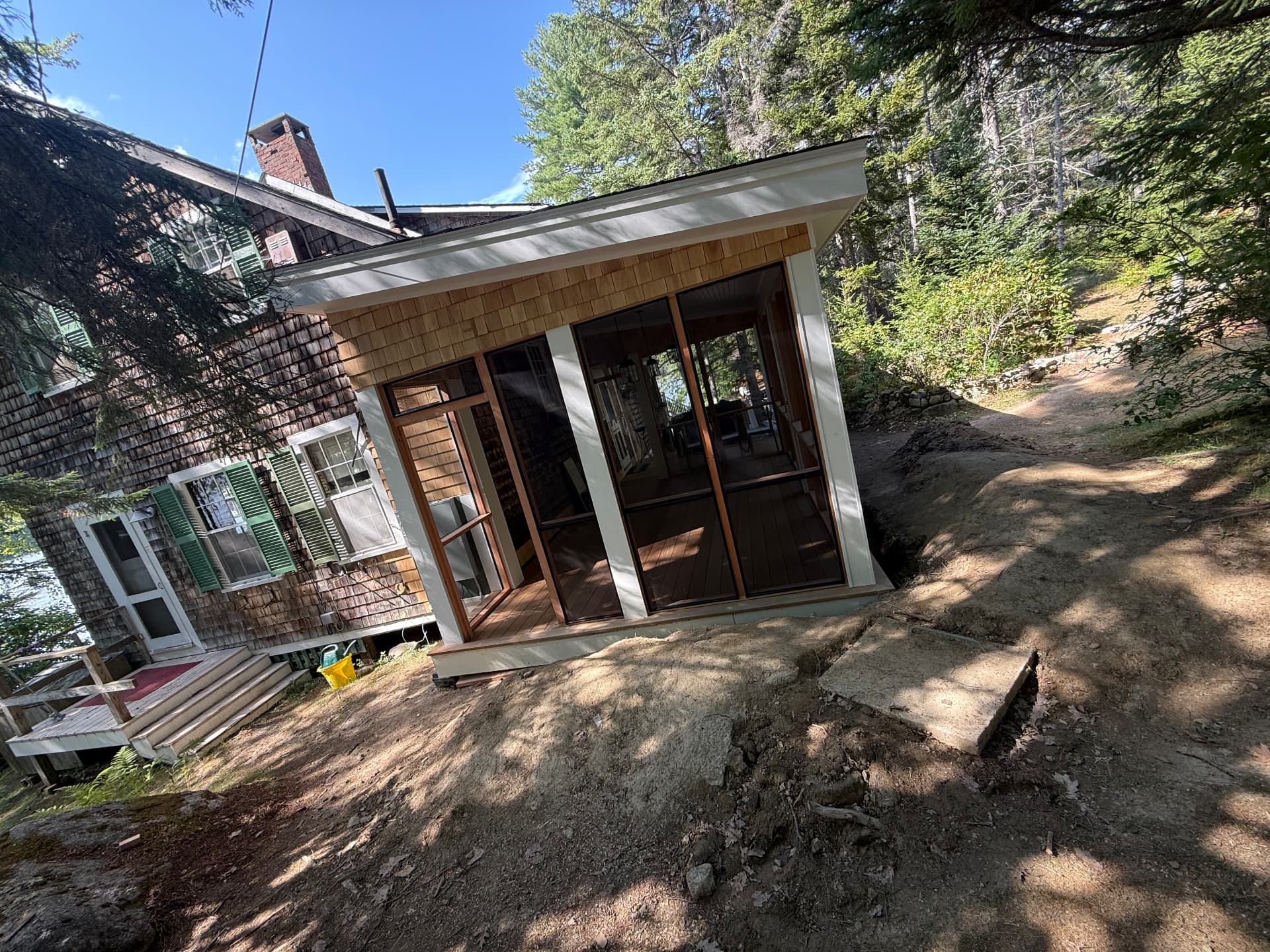Finished screened porch with cedar shingle siding and screen door in the sunshine