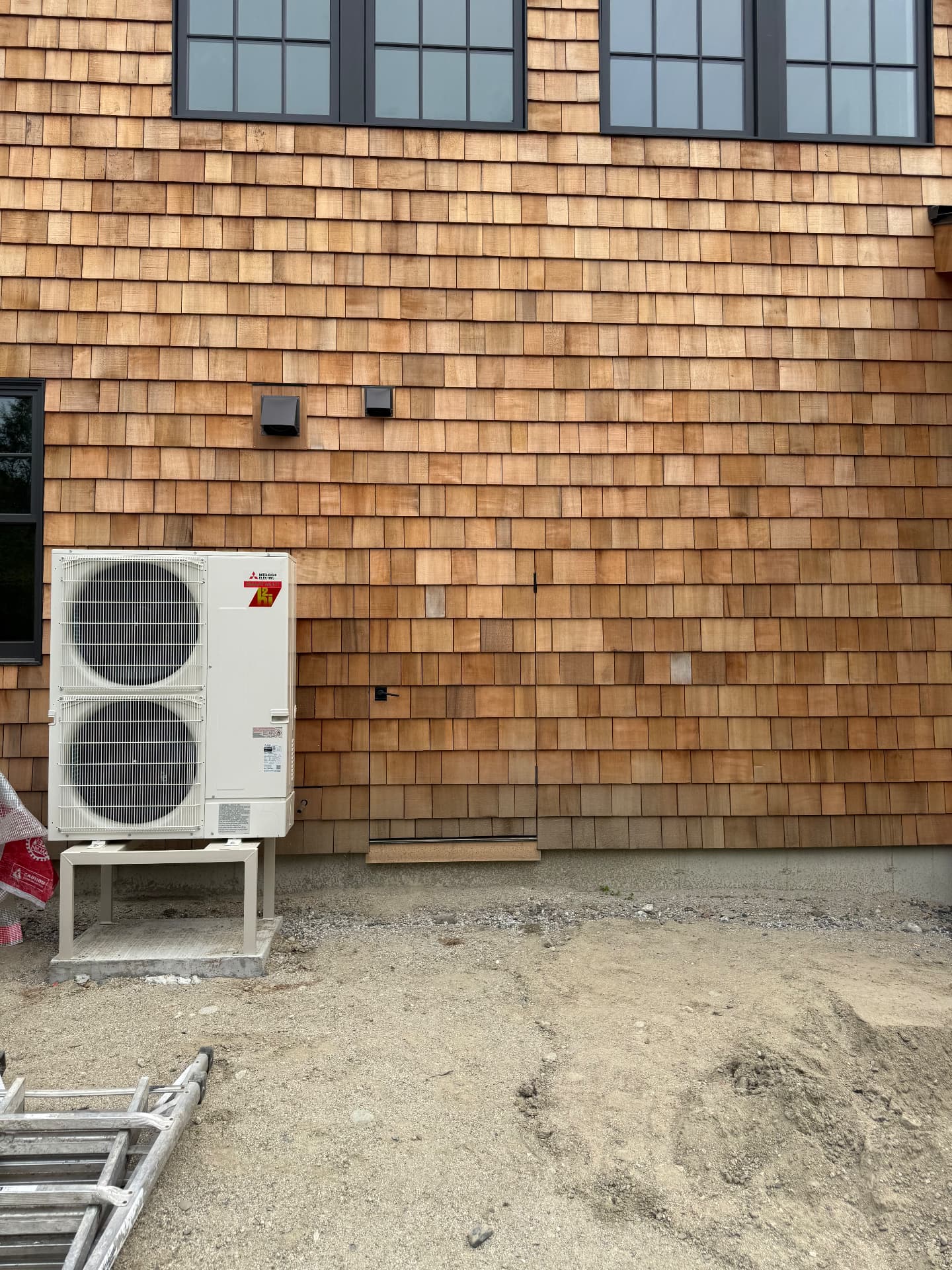 Completed cedar shingle wall with heat pump condenser at a new Maine home