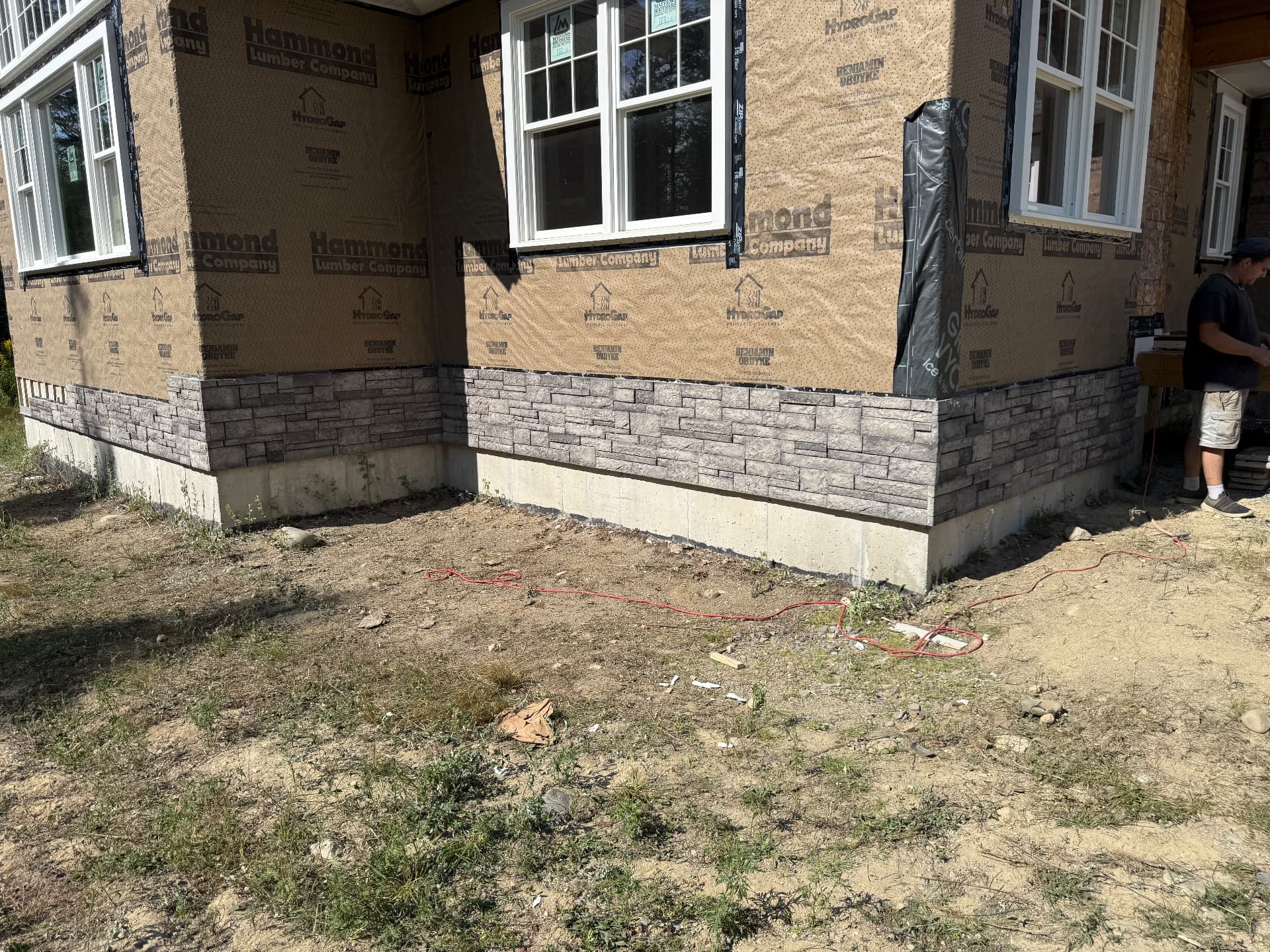 Stone veneer skirting installed over the foundation of a new Maine home still in housewrap