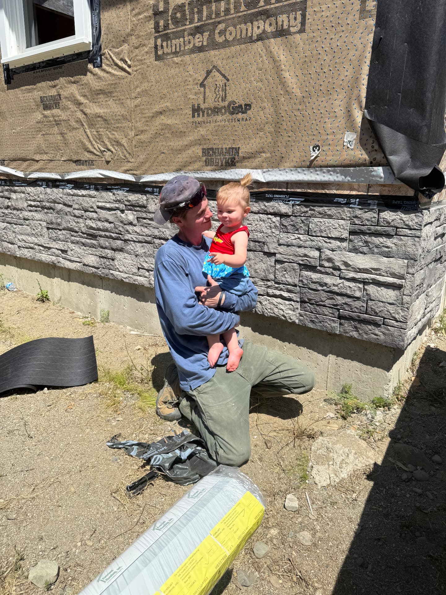 Keith Pomeroy holding his daughter beside the new stone veneer foundation skirting