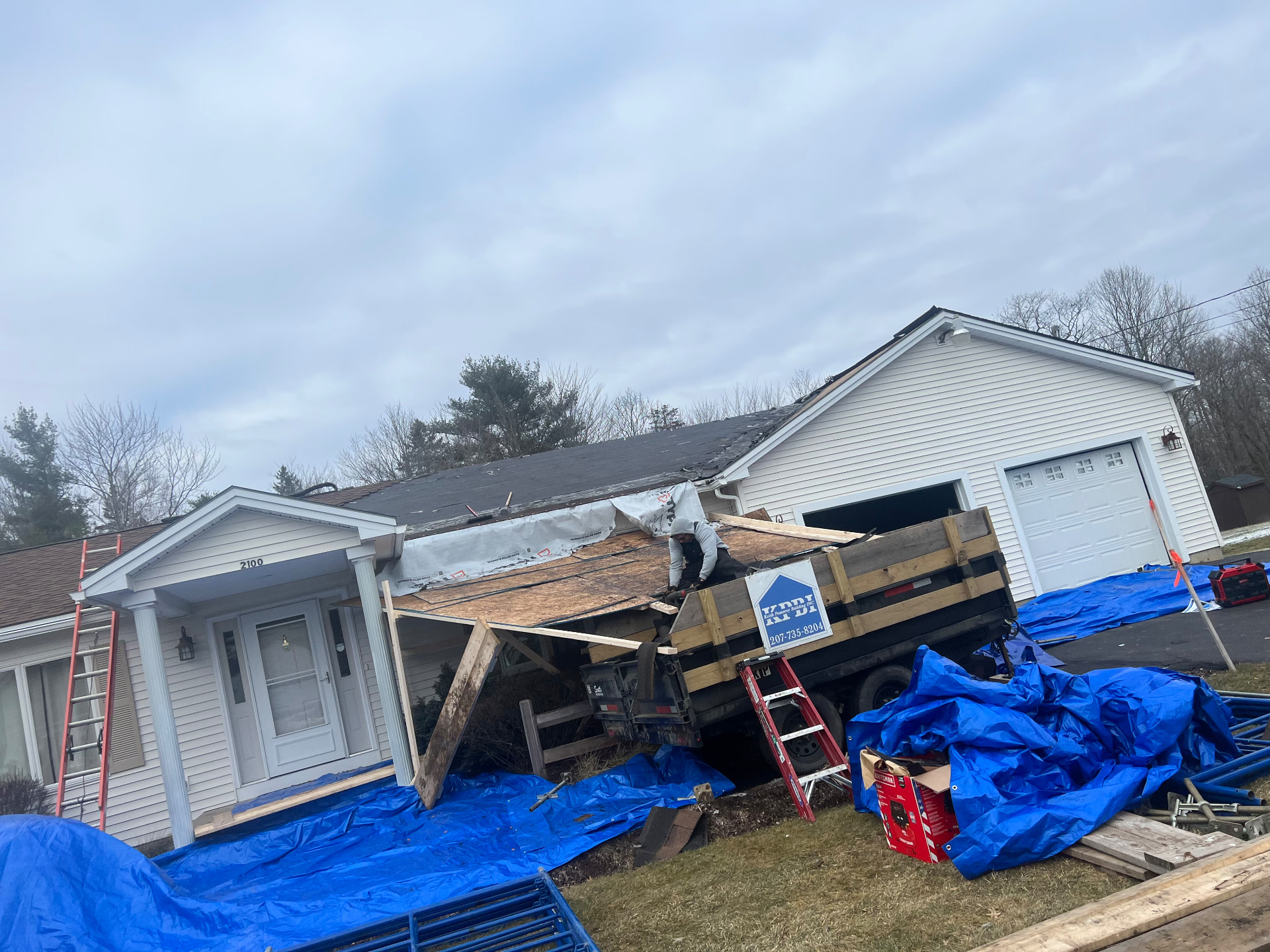 Roof tear-off in progress with dump trailer and tarps protecting a Maine ranch home