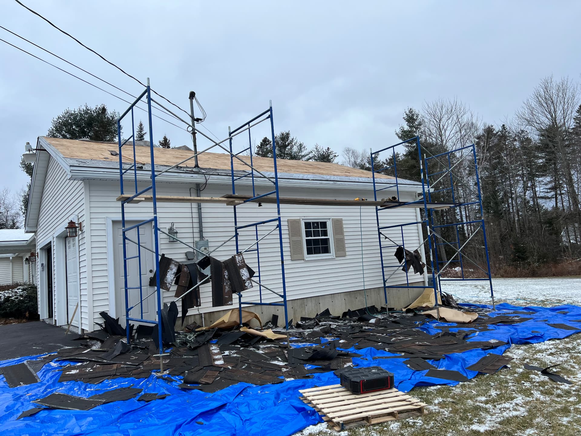 Scaffolding set up and old shingles torn off a garage roof during a Maine winter re-roof