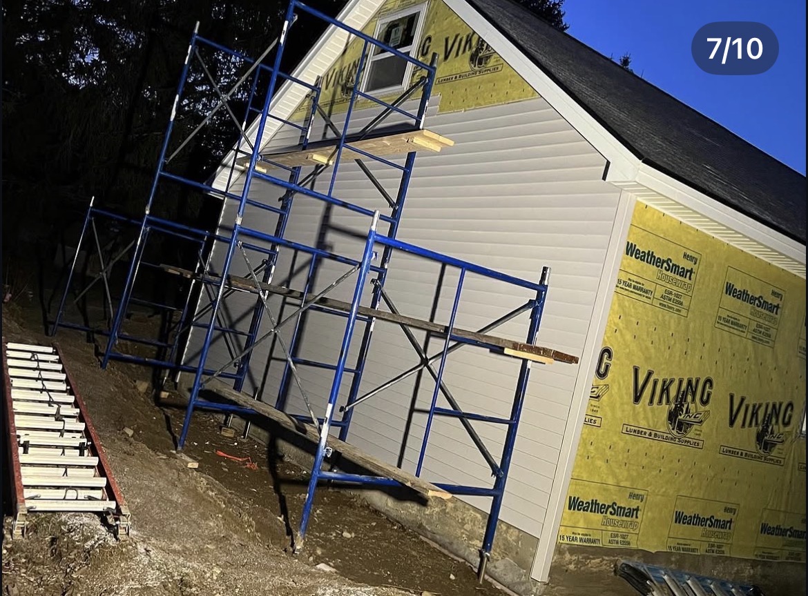 Vinyl siding installation in progress over housewrap with scaffolding at night