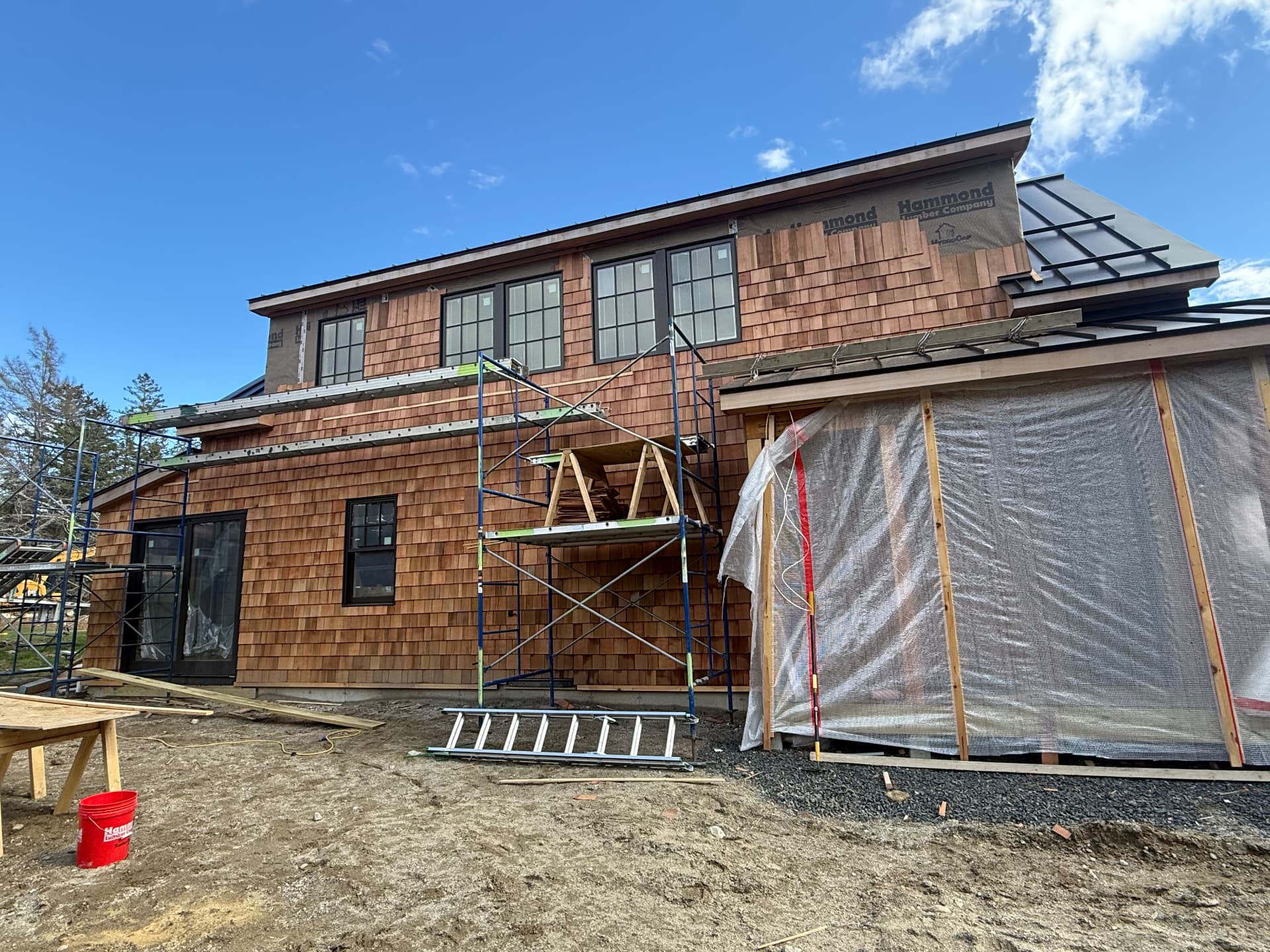 Coastal Maine home being sided in cedar shingles with standing seam metal roof